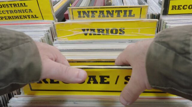 Tracking shot of hands browsing reggae, ska and children&rsquo;s vinyl records in a vintage second hand record store in Spain.