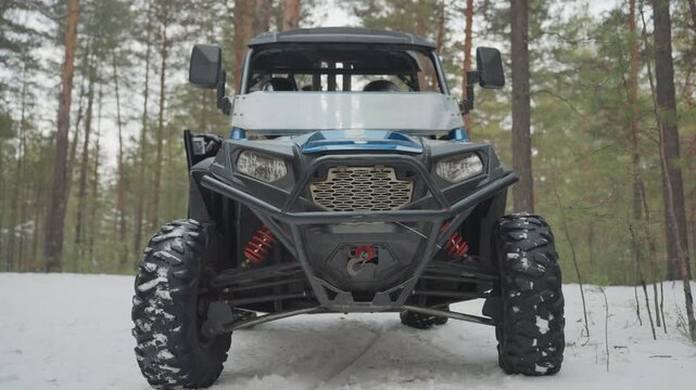 Atv in snowy pine forest, rugged utility vehicle framed by tall conifers, heavyduty bumper with visible winch, aggressive tread tires packed with snow, front grill and illuminated headlights