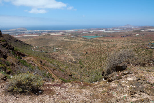 Arid volcanic trail leading towards Cuatro Puertas archaeological site overlooking Gran Canaria coast.