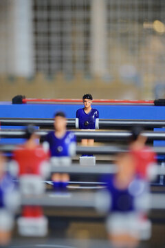 Selective focus on a single blue foosball figure positioned on a rod with blurred figures in the foreground.
