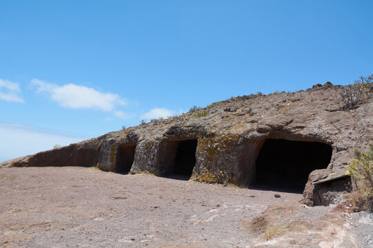 Wide perspective of Cuatro Puertas aboriginal cave entrances hand carved into volcanic stone terrace on hill.
