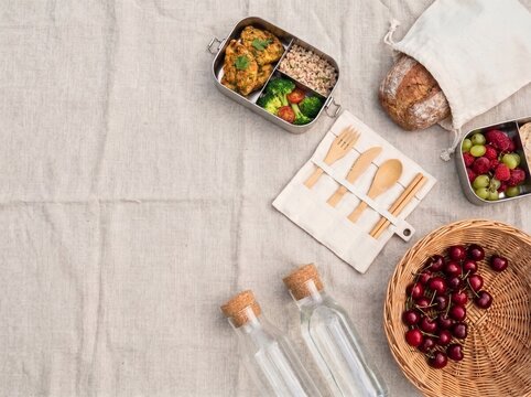 Overhead flat lay of plastic-free picnic essentials with bento boxes, bamboo utensils, and fresh berries on linen