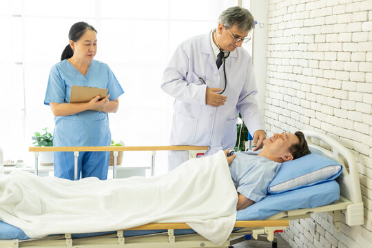 Doctor and nurse with clipboards visiting and checking senior patient man at hospital ward. Medicine, health care and people concept.