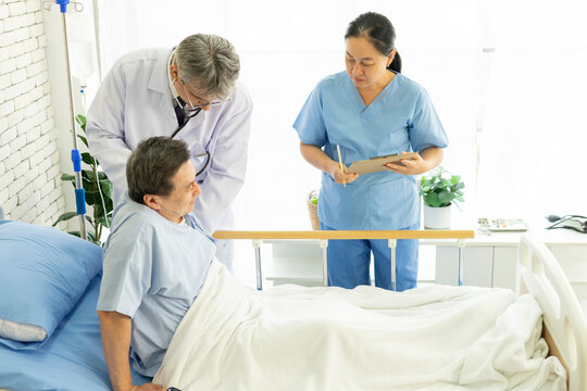 Doctor and nurse with clipboards visiting and checking senior patient man at hospital ward. Medicine, health care and people concept.