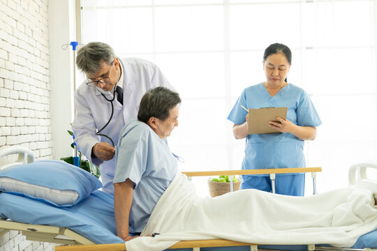Doctor and nurse with clipboards visiting and checking senior patient man at hospital ward. Medicine, health care and people concept.