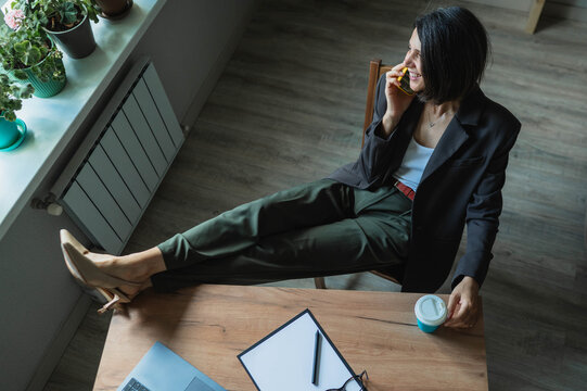 Smiling businesswoman relaxes at desk while talking on smartphone