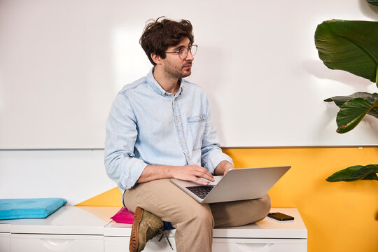 Distracted male employee sits in a modern office using a laptop