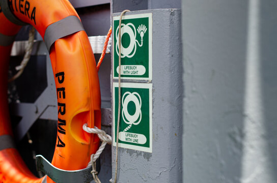 Life buoy mounted on board of the ship vessel adjacent to mandatory safety signage indicating its storage location. The life-saving appliance serves for immediate deployment during a man overboard