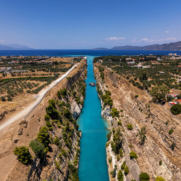 Aerial view of the Corinth Canal with its steep rocky walls and turquoise water, surrounded by olive groves and Mediterranean landscape in Greece.