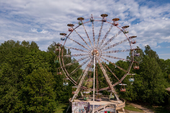 Aerial view of the abandoned Ferris wheel surrounded by lush green trees and graffiti-covered base in Elektrenai, Vilnius County, Lithuania.