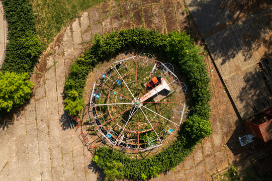 Aerial view of a rusted ferris wheel in an amusement park surrounded by circular hedges and concrete ground in Elektrenai, Vilnius County, Lithuania.