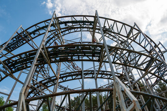 View of the metal structure of a roller coaster ride against a blue sky with clouds and surrounding trees in Elektrenai, Vilnius County, Lithuania.