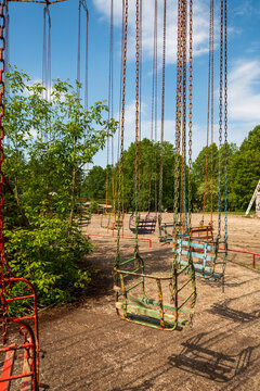 View of a vintage chain swing ride in an amusement park with weathered metal seats and chains under a bright blue sky in Elektrenai, Vilnius County, Lithuania.