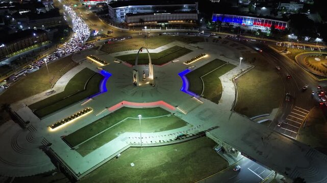 Aerial view of the illuminated Plaza de la Bandera monument at night with surrounding traffic and city lights in Santo Domingo, Santo Domingo Provinc, Dominican Republic.