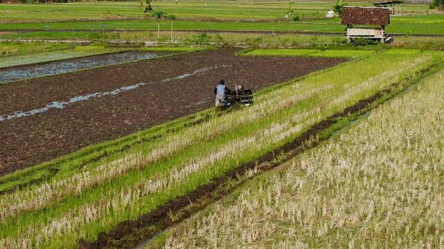 Aerial view of a farmer working with a tiller in a lush rice field near Jalan Bibis in Kecamatan Kasihan, Daerah Istimewa Yogya, Indonesia.