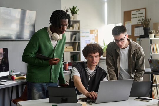 Diverse male students use a laptop together indoors at the university