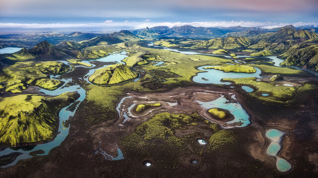 Aerial view of Skafta river winding through vibrant green mossy volcanic hills and turquoise glacial pools in the rugged landscape of Skaftarhreppur, Iceland.