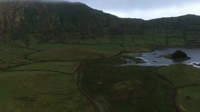 Aerial view of Caldeirao, a volcanic crater lake surrounded by lush green pastures and stone walls on Corvo Island in Vila do Corvo, Azores, Portugal.