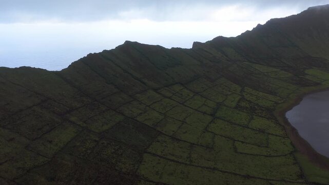 Aerial view of the lush green Caldeirao volcanic crater with its distinct stone wall field patterns on the island of Corvo in Vila do Corvo, Acores, Portugal.