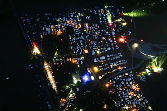 Aerial view of the Grunwald battlefield site at night, illuminated by event lights with numerous tents and crowds gathered on the historic grounds in Grunwald, Warmian-Masurian Voiv, Poland.
