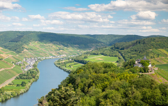Aerial view of the Zeller Hamm loop of the Moselle river, featuring lush vineyards, Petersberg hill, and the Eifel and Hunsrueck mountain ranges in Zell, Rhineland-Palatinate, Germany.