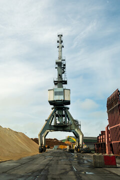 View of a large industrial crane standing near piles of wood chips at the Port of Ventspils in Ventspils, Ventspils Municipalit, Latvia.