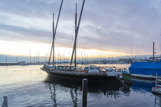 View of a traditional wooden sailboat moored in the harbor at sunset with calm water and a colorful sky in Lausanne, Vaud, Switzerland.