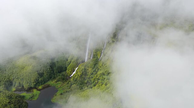 Aerial view of the lush green cliffs and waterfalls at Poco da Ribeira do Ferreiro, shrouded in mist, in Fajazinha, Azores, Portugal.