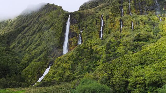Aerial view of the lush green cliffs and multiple waterfalls of Poco da Ribeira do Ferreiro in Fajazinha, Azores, Portugal.