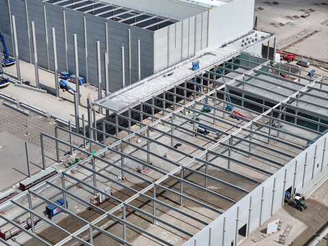 Aerial view of a large industrial construction site featuring a steel frame structure, concrete walls, and various construction vehicles on the ground in the Netherlands.