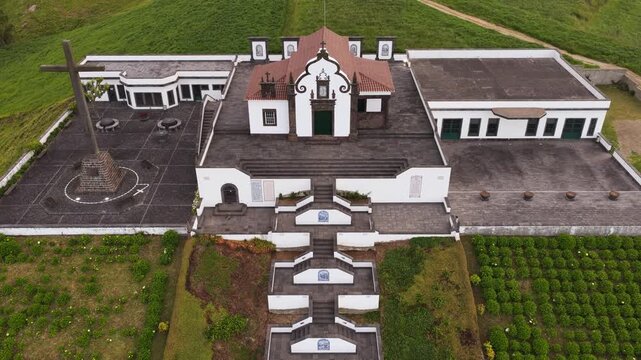 Aerial view of the Sanctuary of Nossa Senhora da Paz with its white facade, dark stone stairs, and courtyard in Vila Franca do Campo, Acores, Portugal.