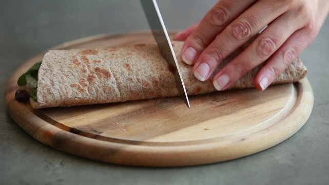 Female Hands Preparing Mediterranean Greek Wrap with Hummus, Feta, Cucumber, and Olives