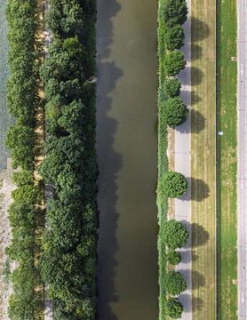 Aerial view of a straight canal lined with lush green trees and a paved path running alongside in Middenmeer, North Holland, Netherlands.