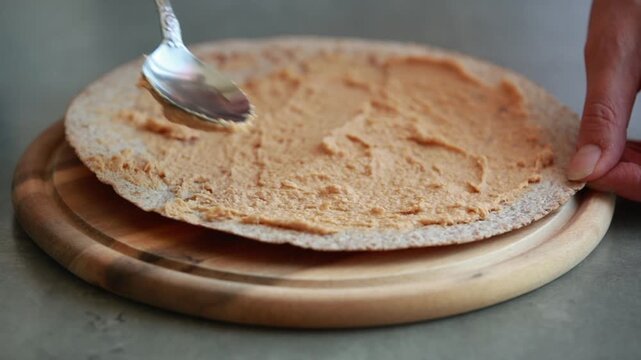 Spreading Fresh Hummus on Baked Whole Wheat Flatbread on Wooden Cutting Board