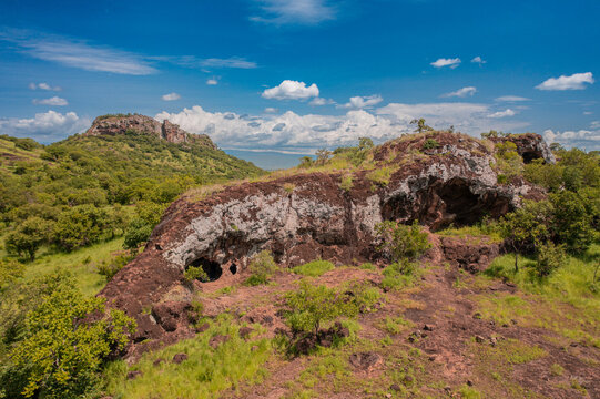 View of the rocky landscape and caves at Pian Upe Game Reserve in the savanna, with green trees and a blue sky in Namalu, Northern Region, Uganda.