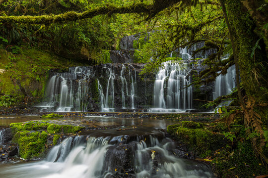 View of Purakaunui Falls cascading over moss-covered rocks surrounded by lush temperate rainforest in Purakaunui, Otago Region, New Zealand.
