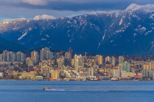 Panoramic view of Vancouver skyline with snow-capped mountains, waterfront, and a small motorboat