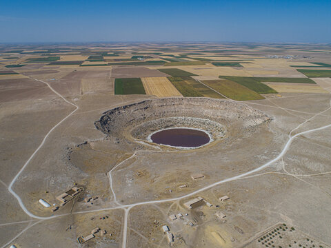 Aerial view of Meyil Lake, a circular sinkhole with reddish water surrounded by arid plains and agricultural fields in Karapinar, Konya, Turkiye.