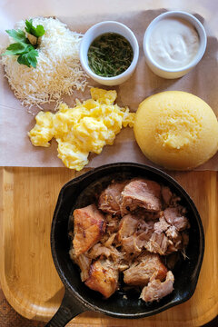 Traditional Moldovan food on a wooden board: mamaliga made from cornmeal, fried meat, feta cheese, garlic sauce, and sour cream. National village food. Close-up. View from above.