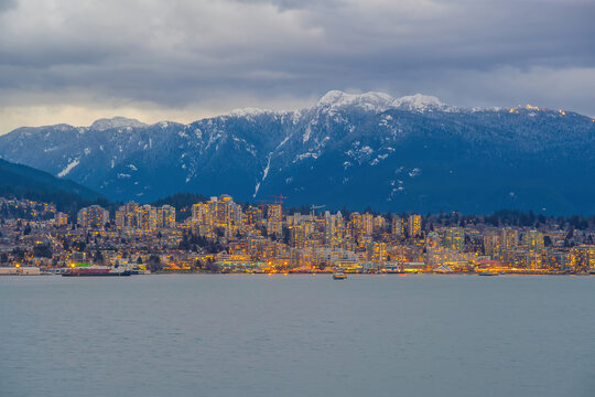 Panoramic view of Vancouver skyline with snow-capped mountains, waterfront, and a small motorboat