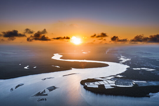 Aerial view of Pontal da Barra do Mamanguape estuary at sunset, with winding river channels, lush mangroves, and golden light reflecting on the water in Rio Tinto, State of Paraiba, Brazil.