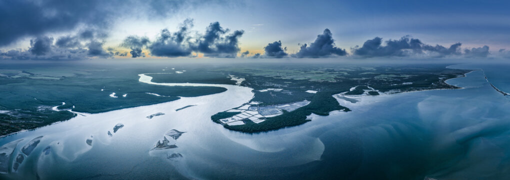 Aerial view of Pontal da Barra do Mamanguape where the river meets the Atlantic Ocean, with lush mangroves, sandbanks, and a dramatic cloudy sky in Rio Tinto, State of Paraiba, Brazil.