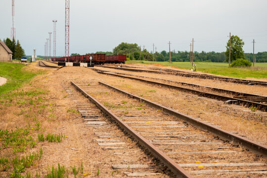 View of railway tracks leading to a freight train in the distance with power lines and green fields in Pakruojis, Siauliai County, Lithuania.