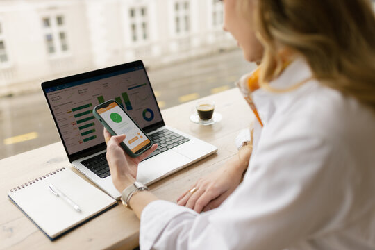 Woman analyzes finance on laptop and checks smartphone at desk