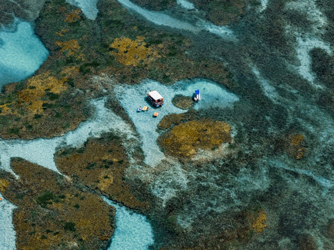 Aerial view of Piscinas naturais em Ponta do Seixas featuring vibrant coral reefs and turquoise waters with small boats anchored in Joao Pessoa, Paraiba, Brazil.