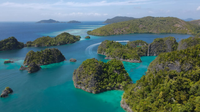 Aerial view of Raja Ampat with lush green karst islands surrounded by turquoise waters and a speedboat leaving a wake in Raja Ampat, Southwest Papua, Indonesia.