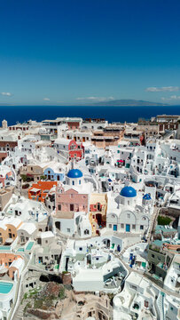 Aerial view of the iconic white buildings and blue-domed churches of Oia, Santorini, with narrow streets and the Aegean Sea in the background in Oia, Greece.
