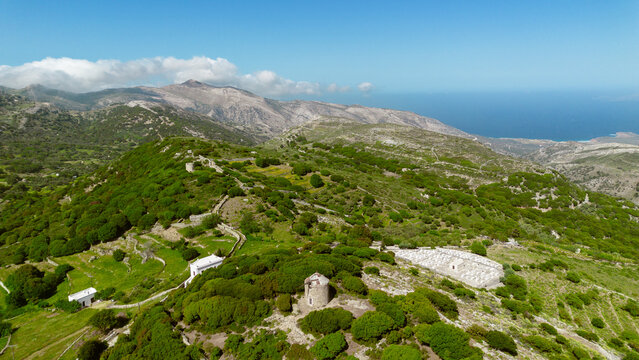 Aerial view of the historic village of Apeiranthos surrounded by lush green mountains, stone walls, and ancient windmills in Apeiranthos, Greece.