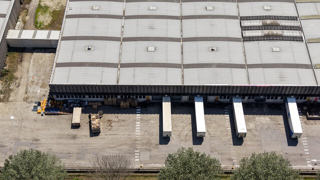 Aerial view of a large logistics warehouse complex with loading docks and parked semi-trailers in Caleppio, Lombardy, Italy.