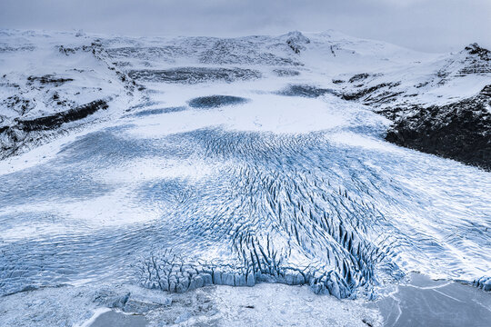 Aerial view of Fjallsarlon glacier with deep blue crevasses and surrounding snow-covered mountains in Sveitarfelagid Hornafjordur, Iceland.